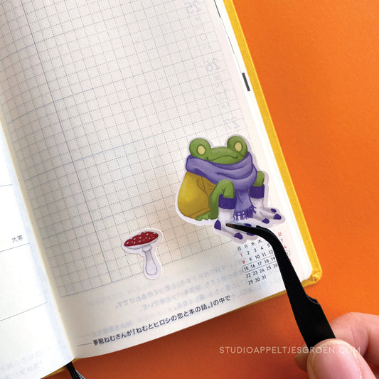 a planner page being deocrated by a sticker of a frog in a sweater with a small mushroom next to it.