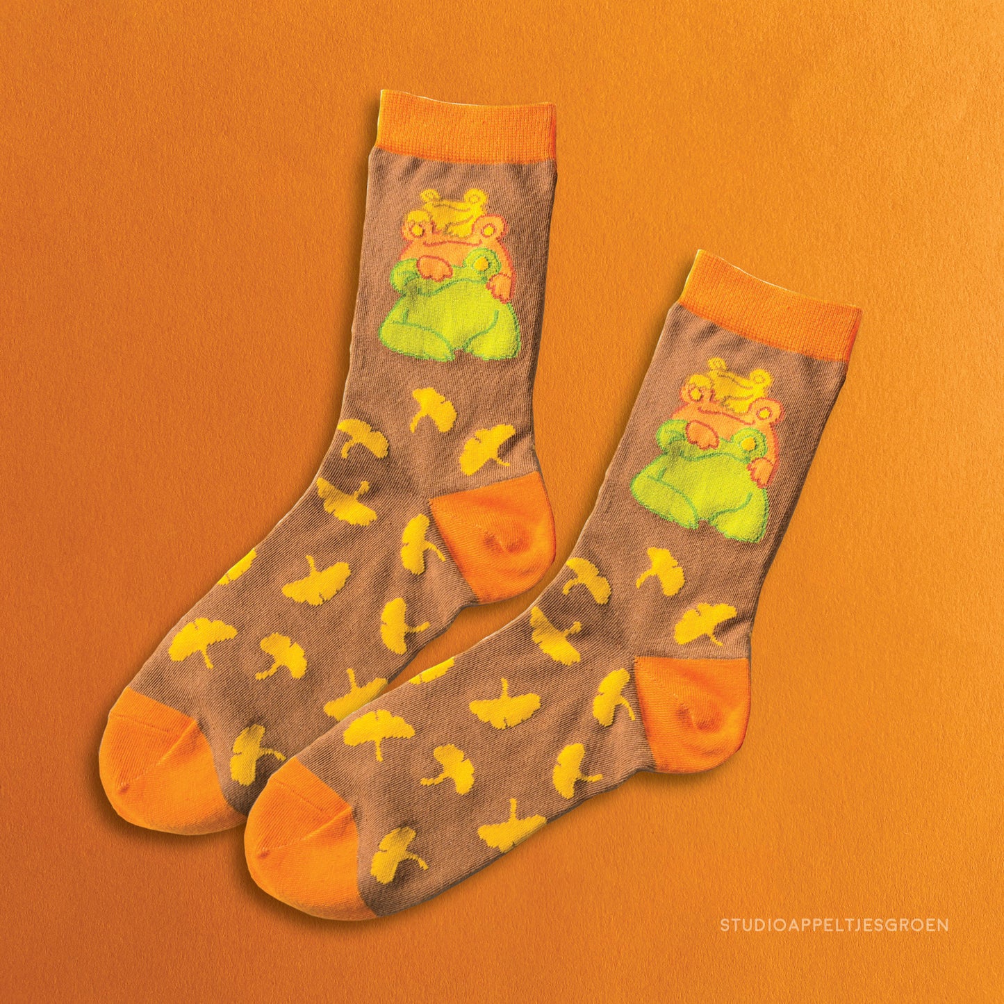 Orange with brown socks depicting three frogs stacked on top of each other, with a yellow ginkgo leaves pattern