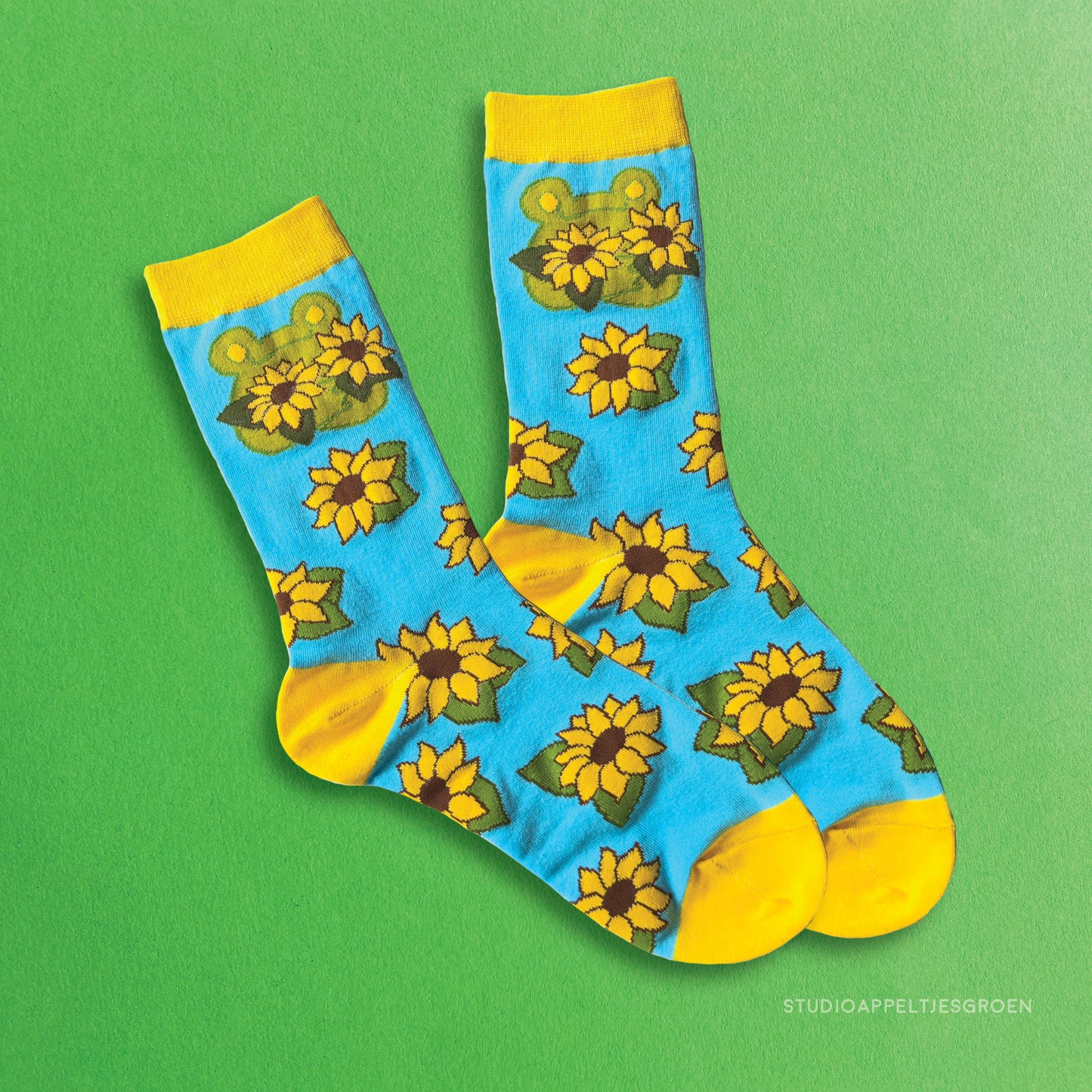 Frog socks in bright blue and yellow depicting a frog holding up two sunflowers and a pattern of other sunflowers on the rest of the sock